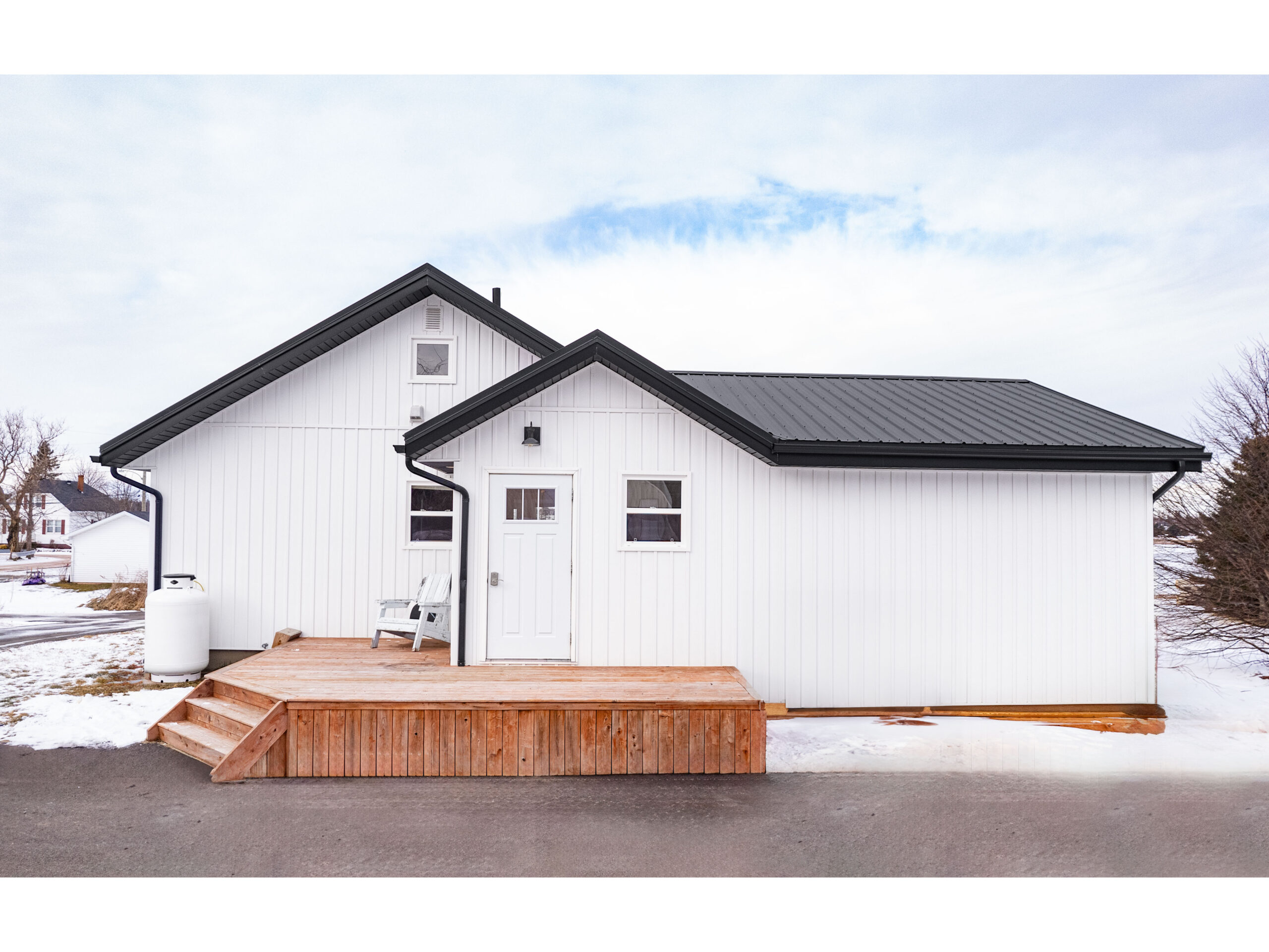 A small deck extends off the back of a small white house with a black roof.