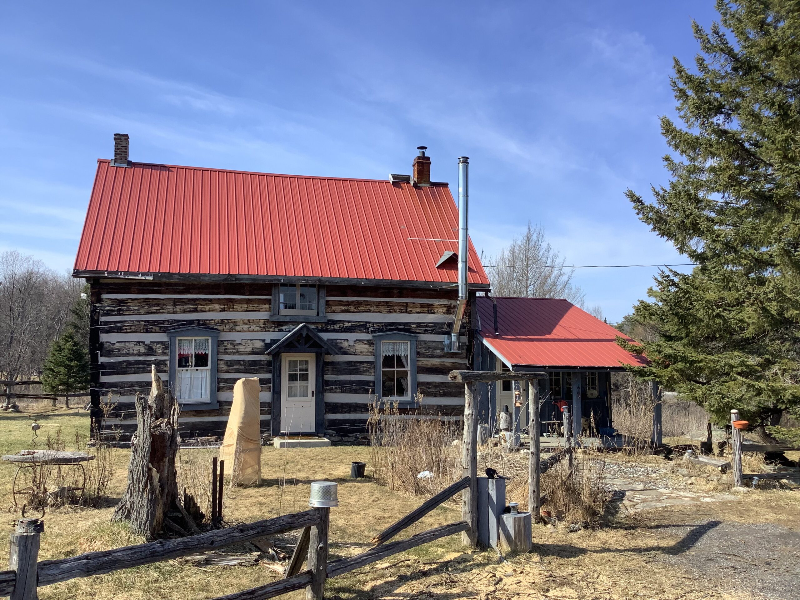 A small wood farmhouse with a red roof and a white door. The wood is white and grey, in a rustic horizontal striped pattern.