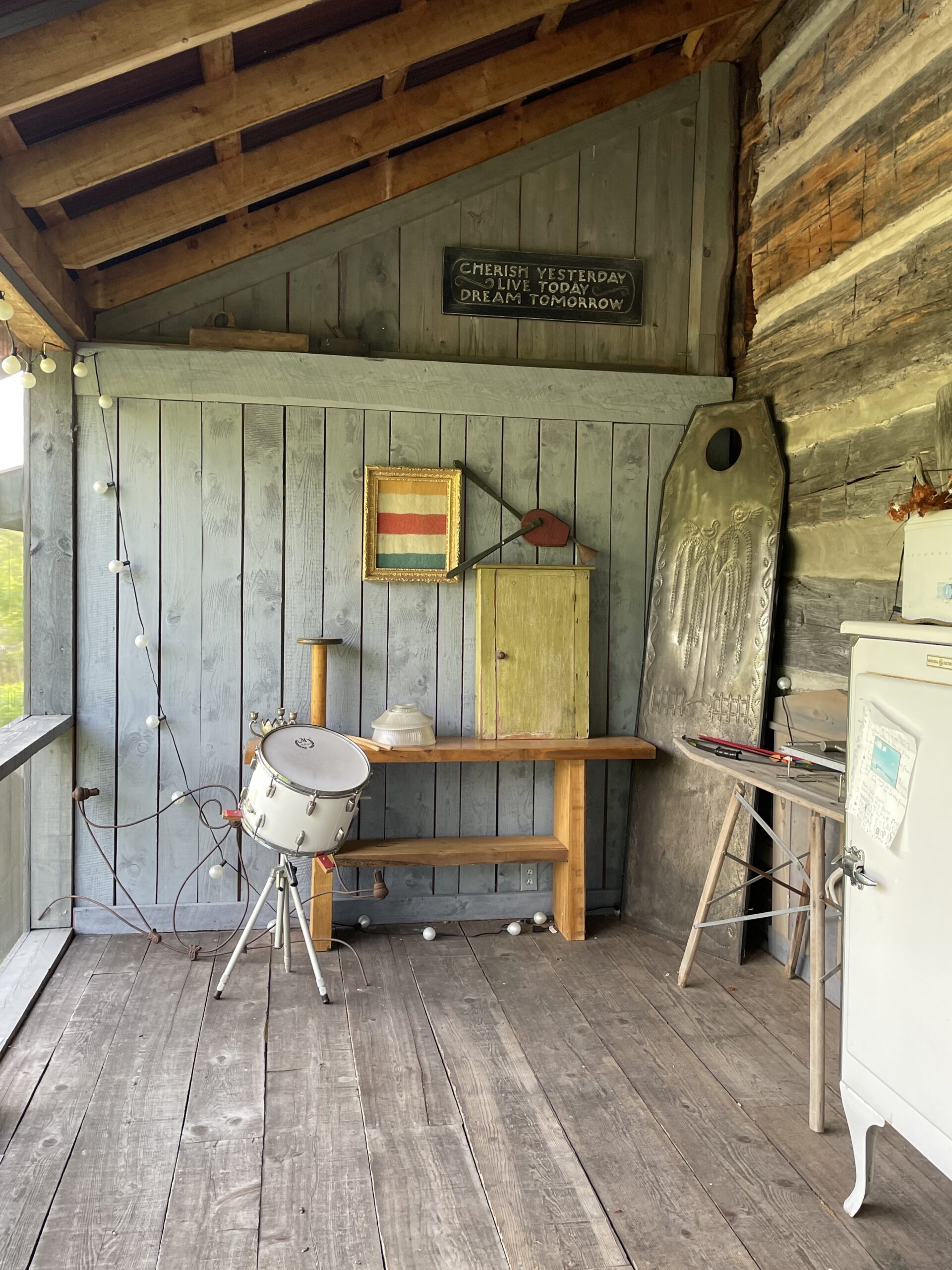 A screened-in porch with mismatched items such as a drum, a shelf, an ironing board, and a small white hutch.