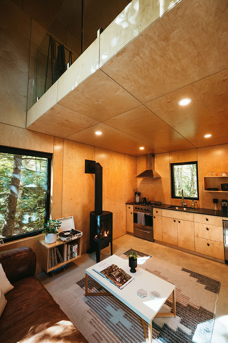 A brown leather couch faces the coffee table, wood stove, and kitchen.
