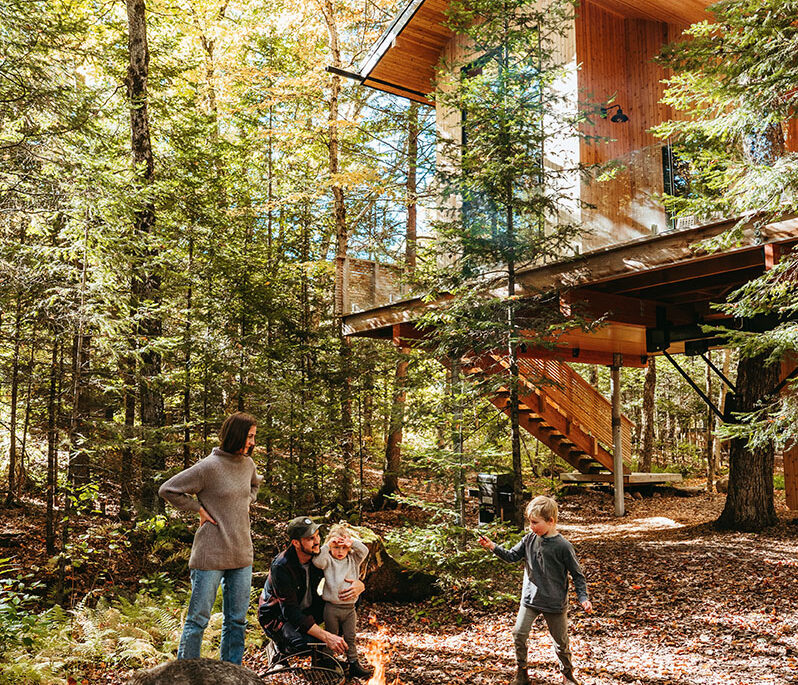 Lauren, Cam, and their kids stand around a fire in front of their treehouse cabin