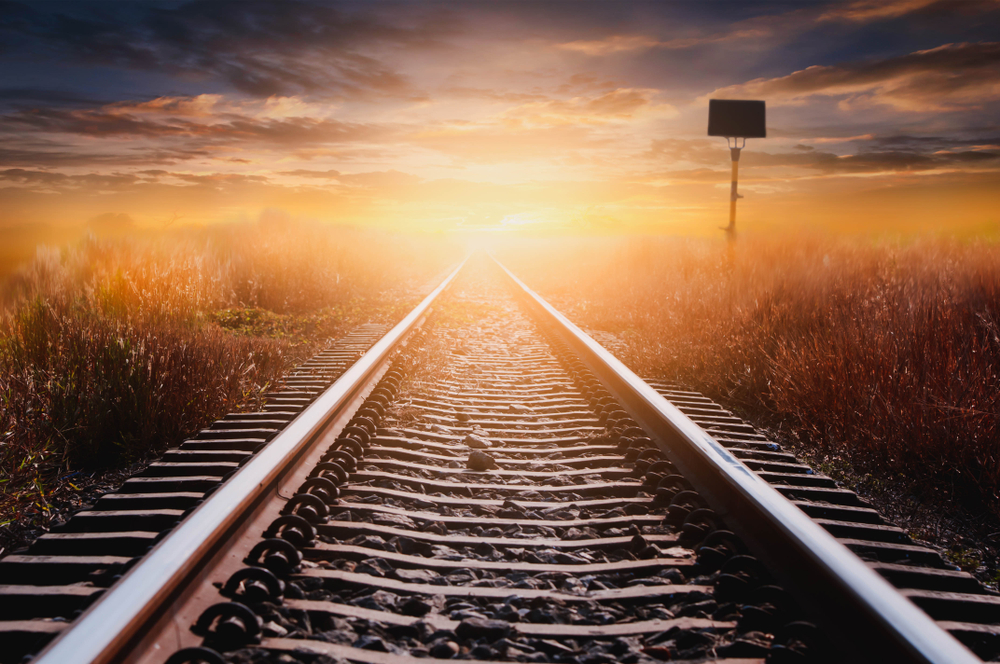 The sun's rays hitting a train track that cuts through grassland