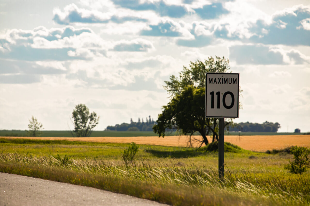 A street sign reads "Maximum 110" on a road in the praries