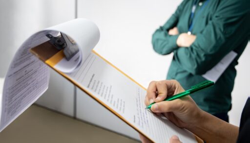 Inspector writting on a clipboard. Man in the background with arms crossed. Heat pump installation gone wrong