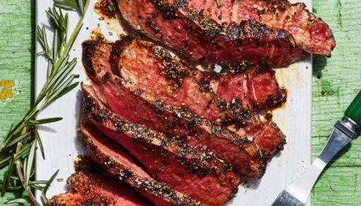 Sliced steak on a white plate with a small green bowl of spice