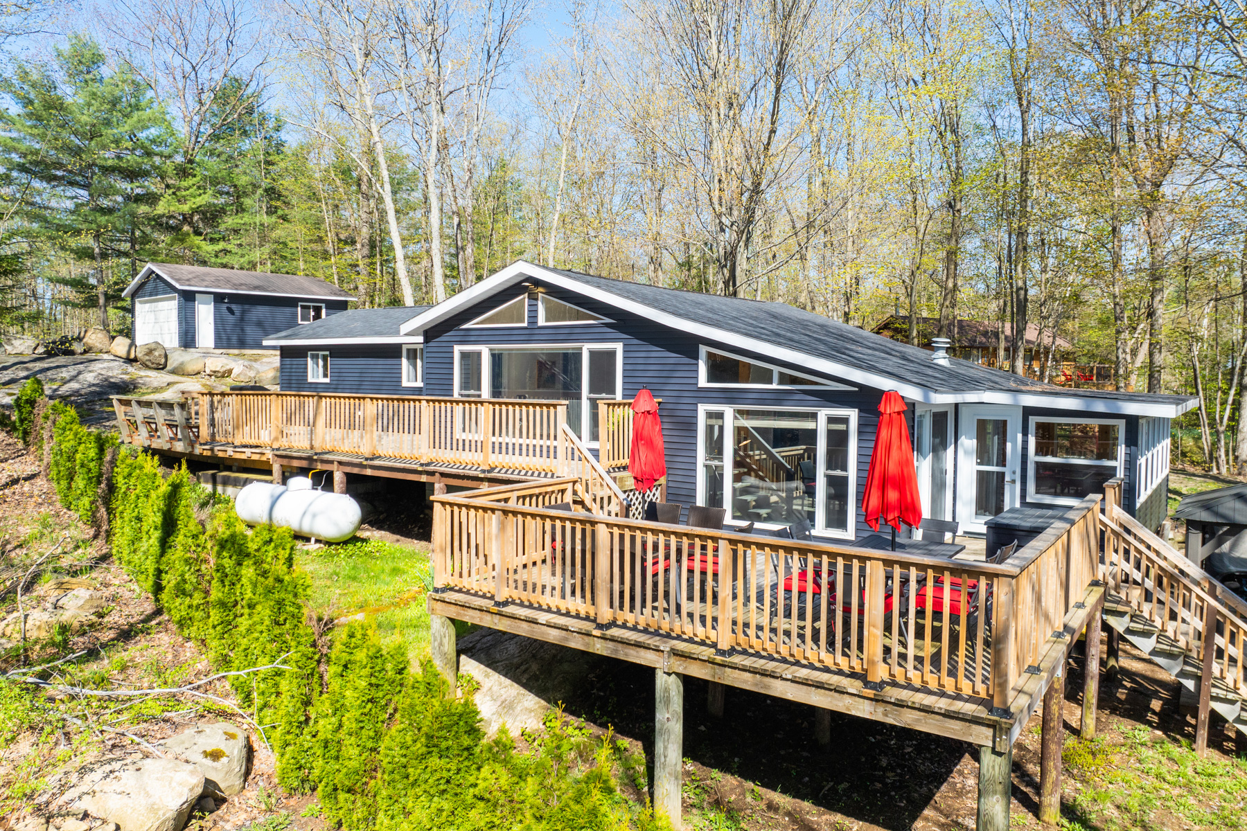 A large cottage bungalow with navy blue exterior siding, big windows, and a large two-level wooden deck with an outdoor dining area.