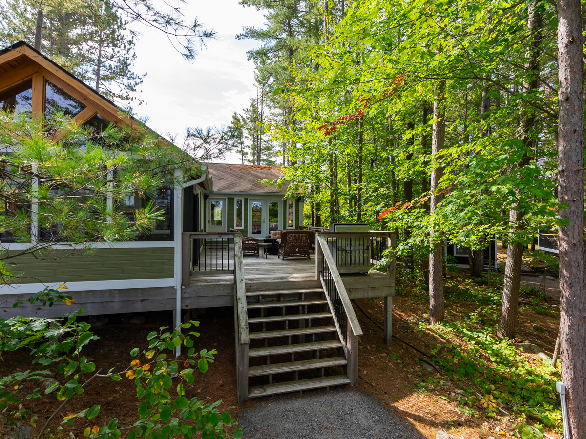The back of the cottage has large windows, attached is a large deck with stairs that lead down to the property