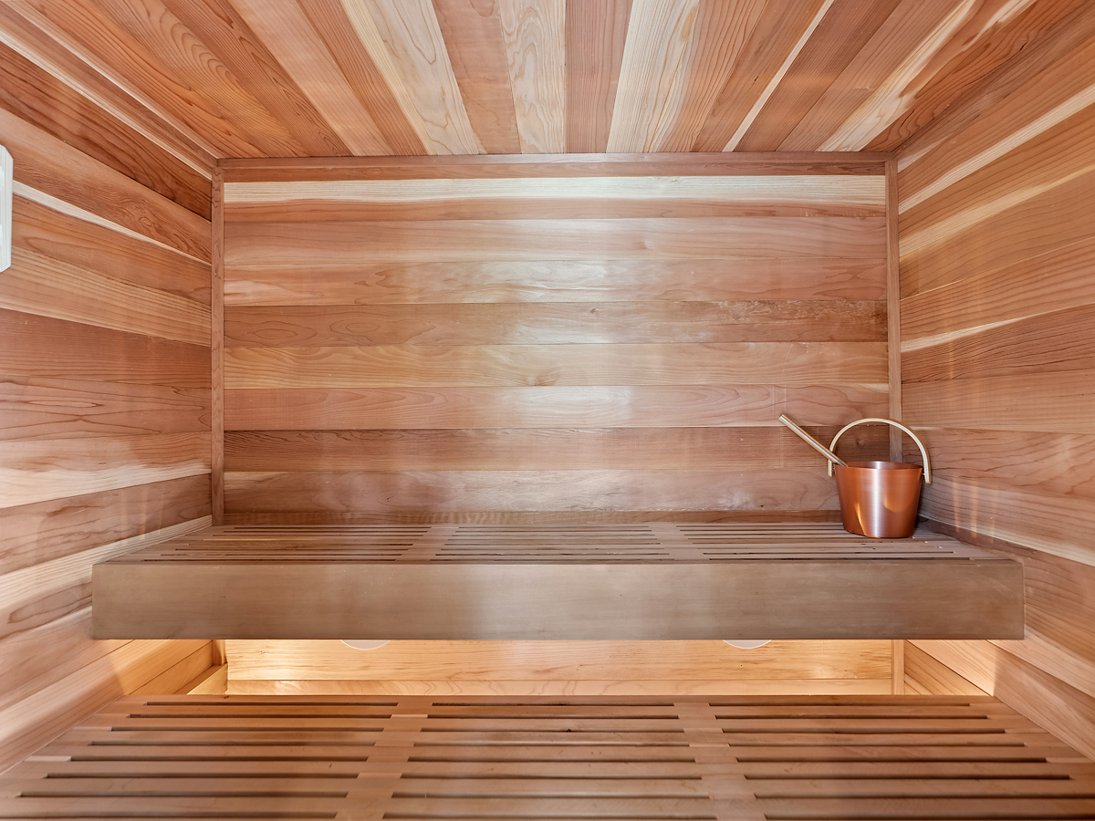 Cedar sauna with a wood bench and copper water can