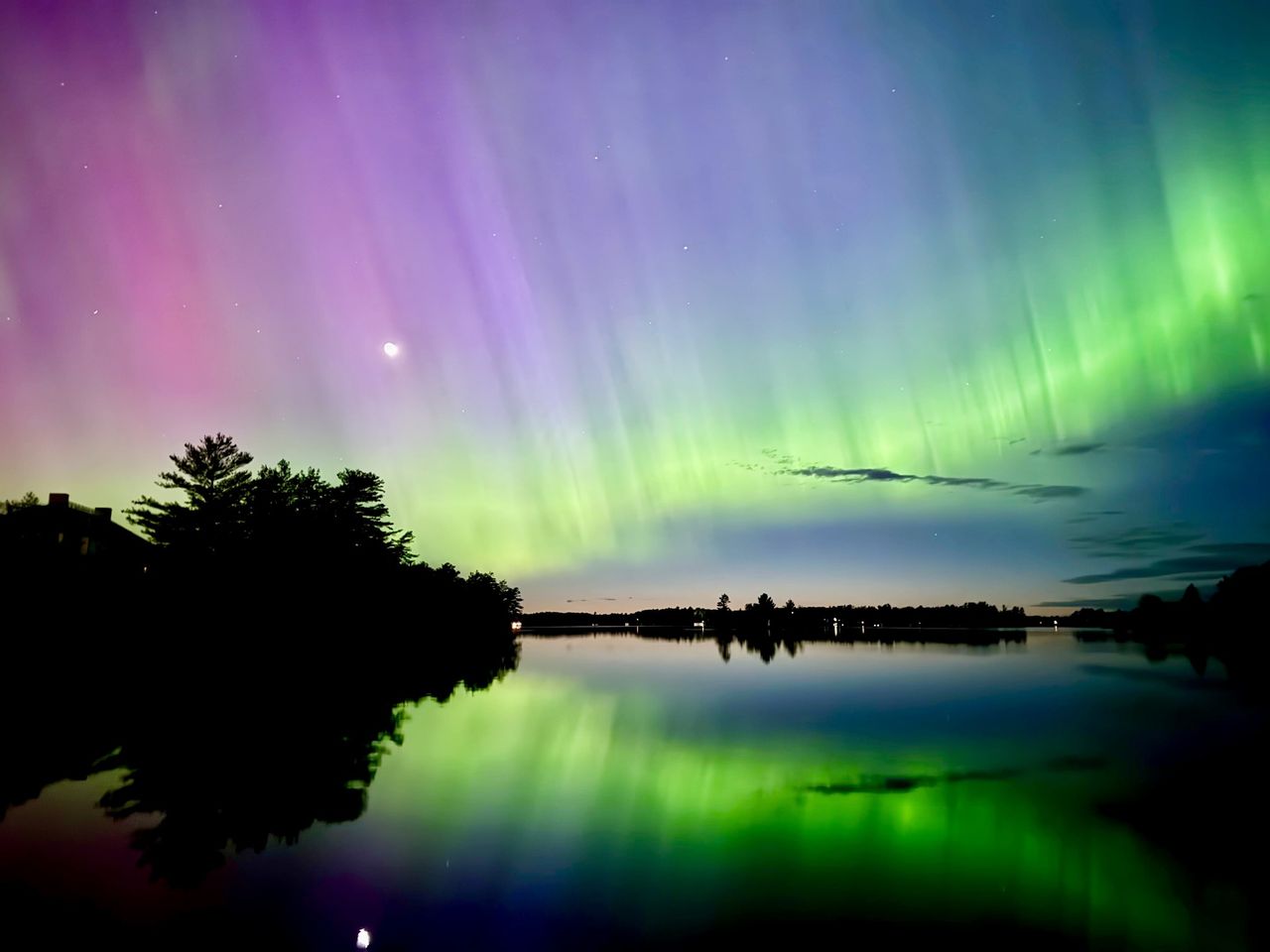 Northern lights over a lake with tree silhouettes