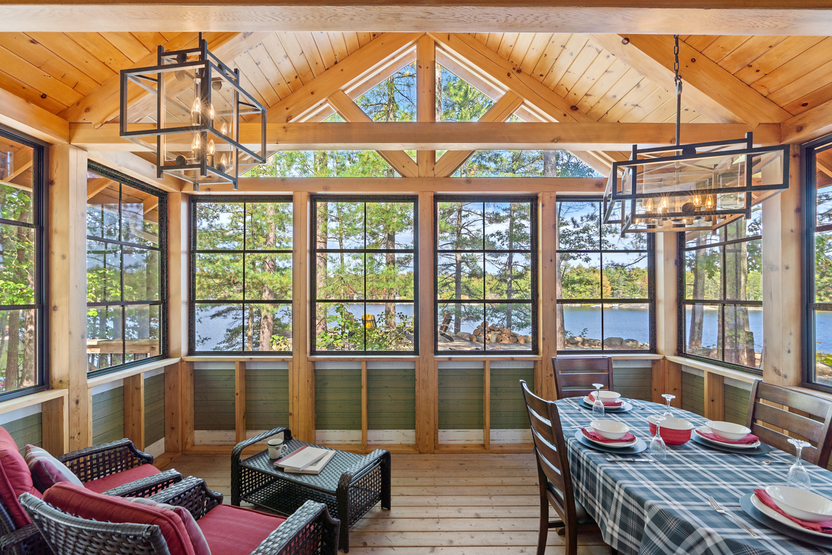 A sun room with large windows has a small lounge area to the left and a dining table to the right