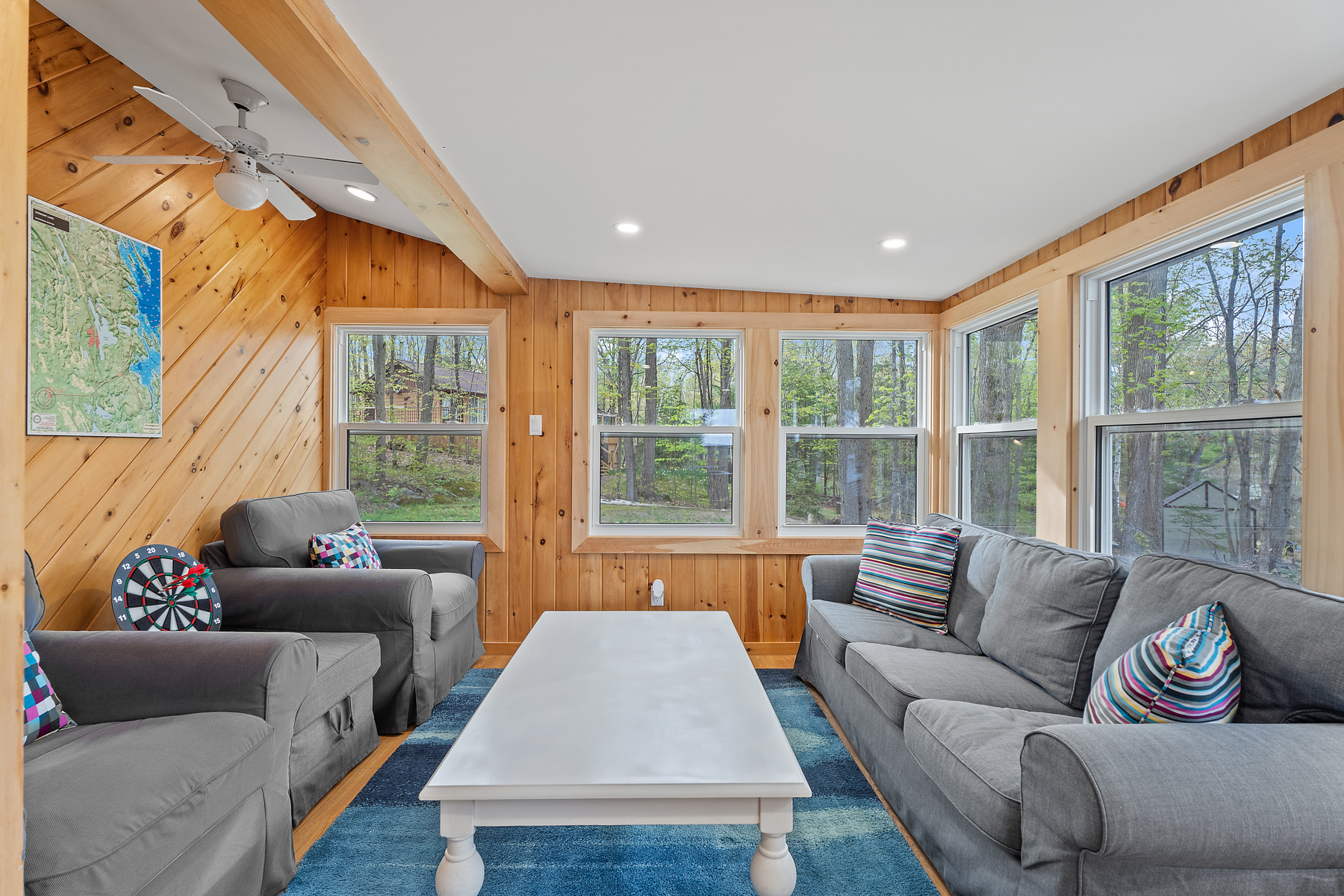 A sunroom with a couch, two chairs, a coffee table, and lots of windows on wood-panelled walls.