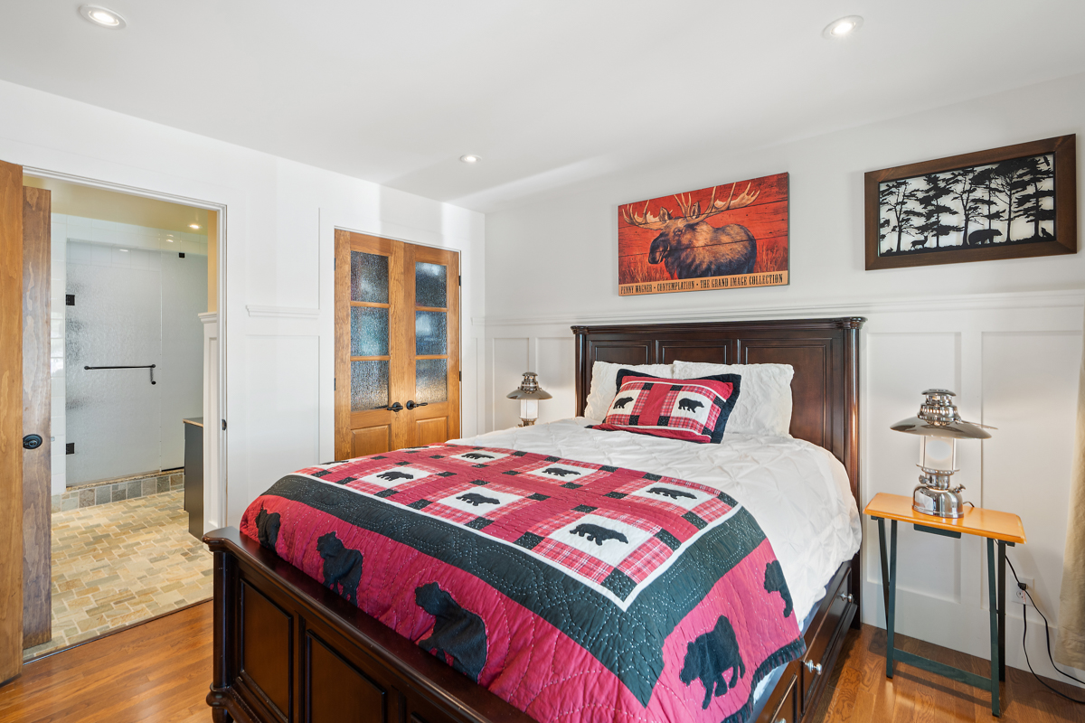 Brown bedframe with a red bedspread, paintings above the bed, ensuite bathroom to the left