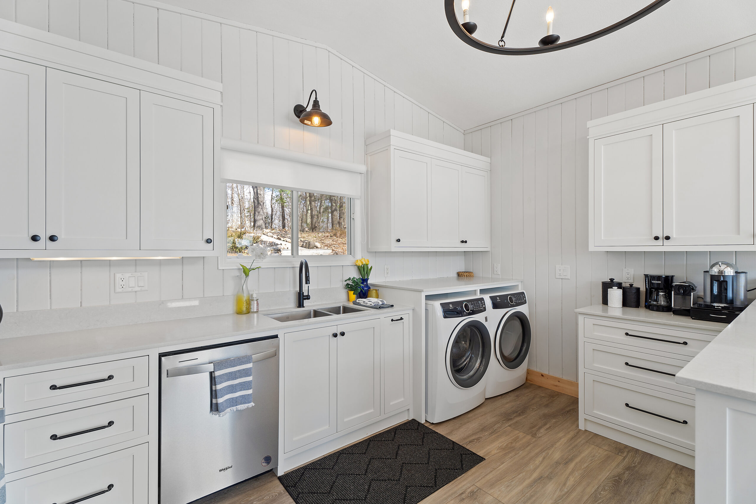 A white wall of the kitchen with the silver dishwasher and white laundry machines