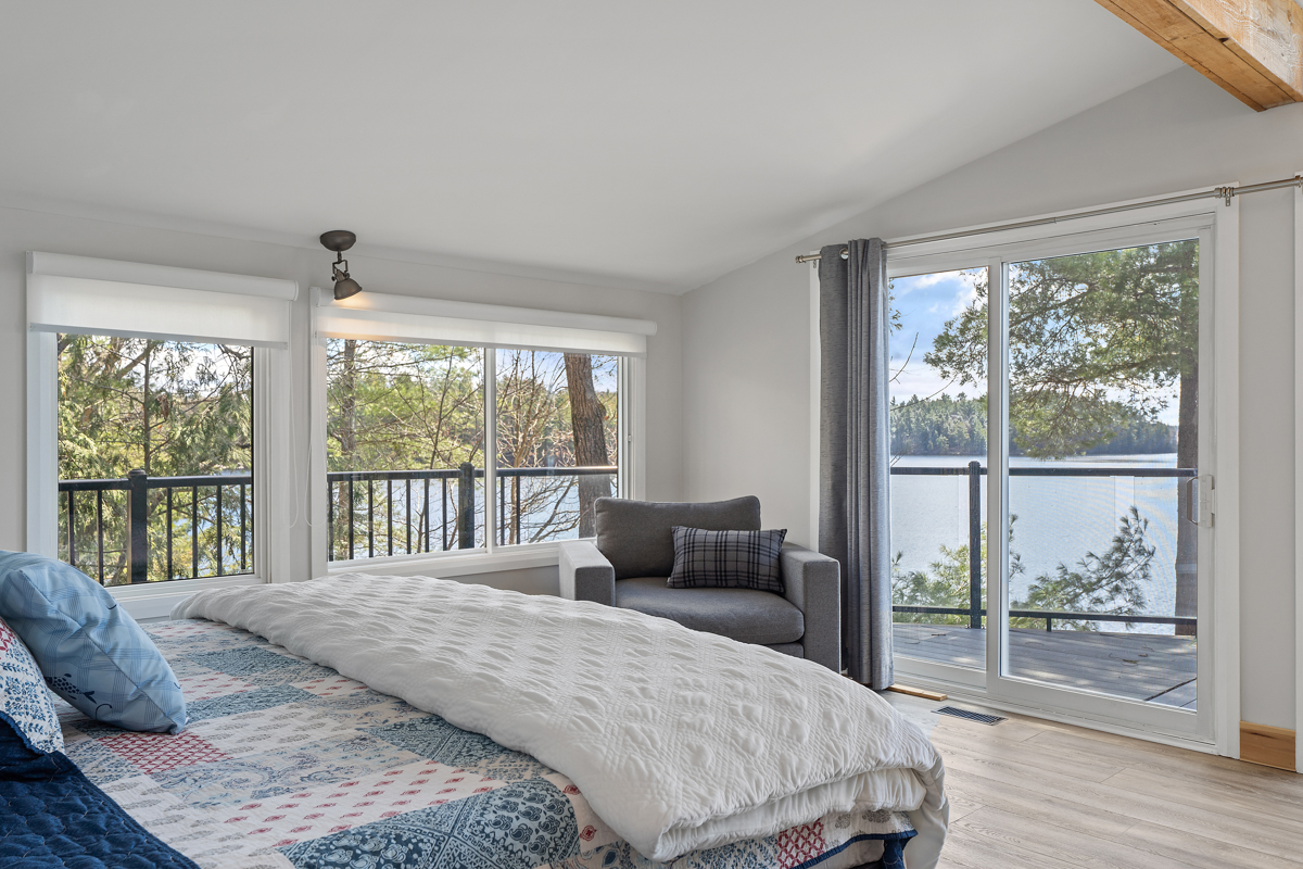 A quilted bed faces a grey loveseat and glass sliding doors