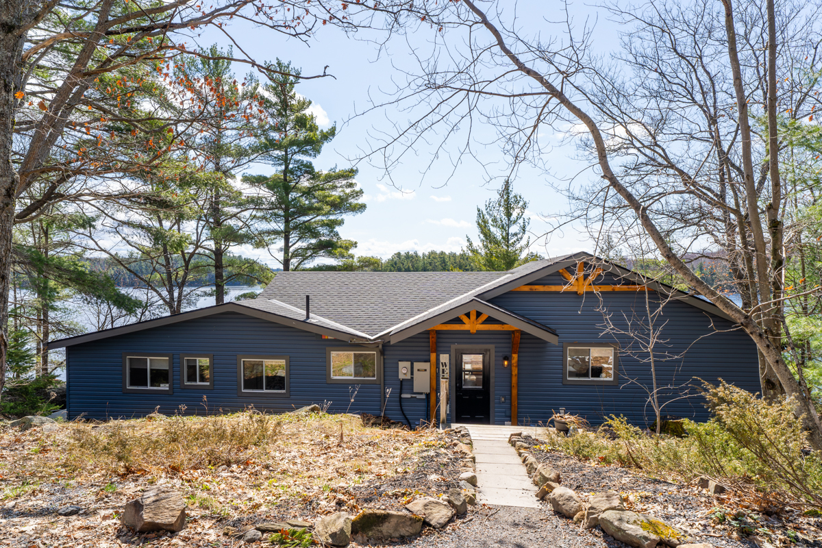 Outside of the front of the blue cottage has a path leading to the door surrounded by brown grass