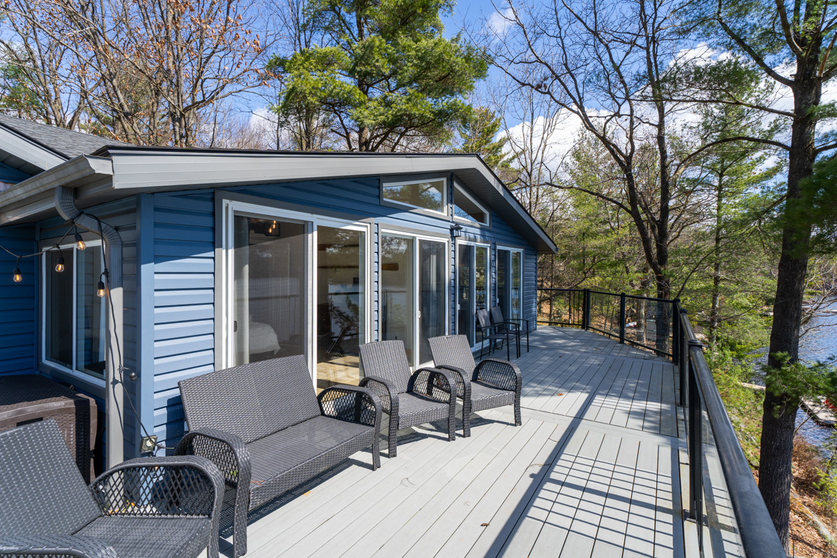 Reverse view of deck, a seating area of grey chairs outside the glass back of the cottage