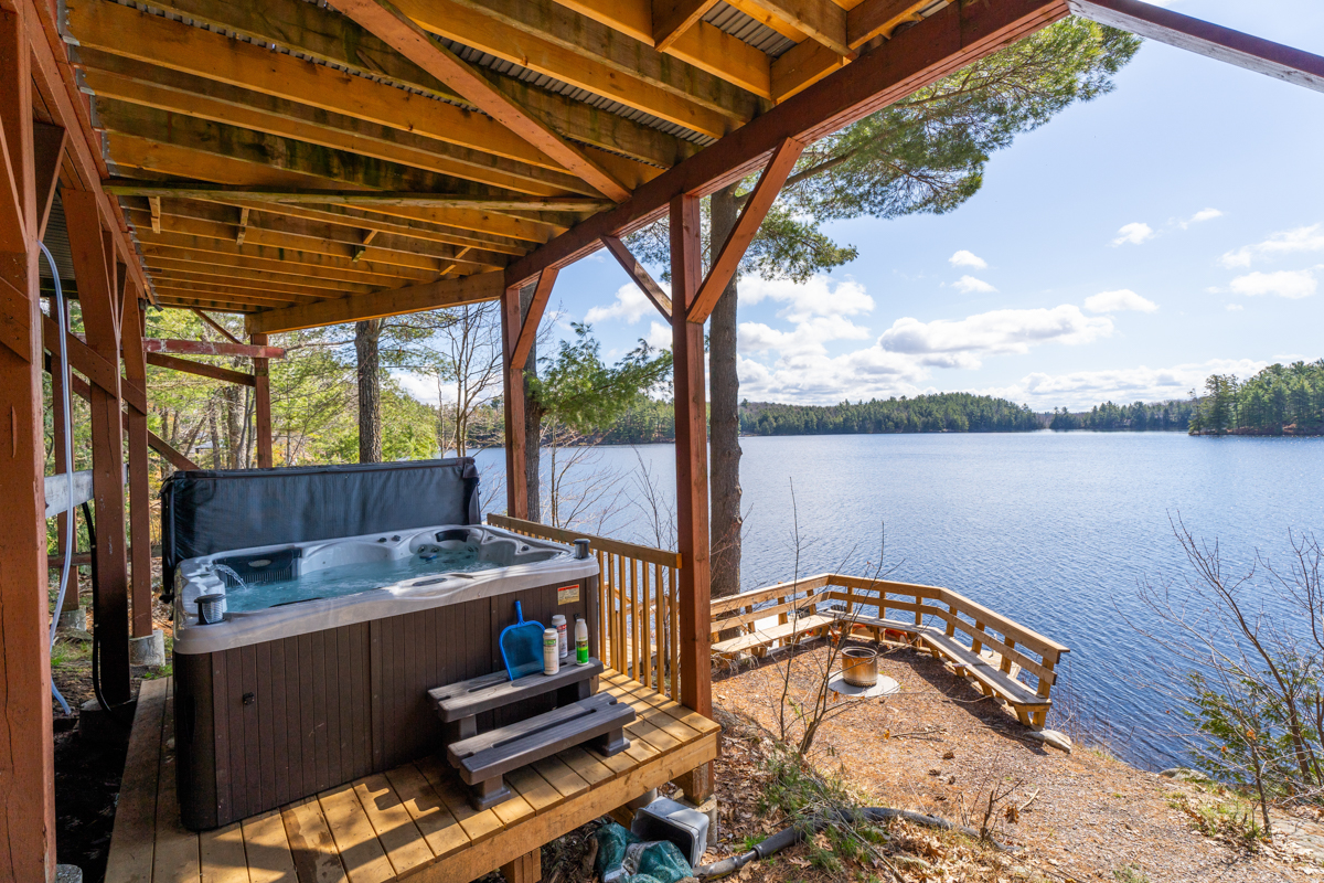 A partially covered hot tub covered by a wood gazebo