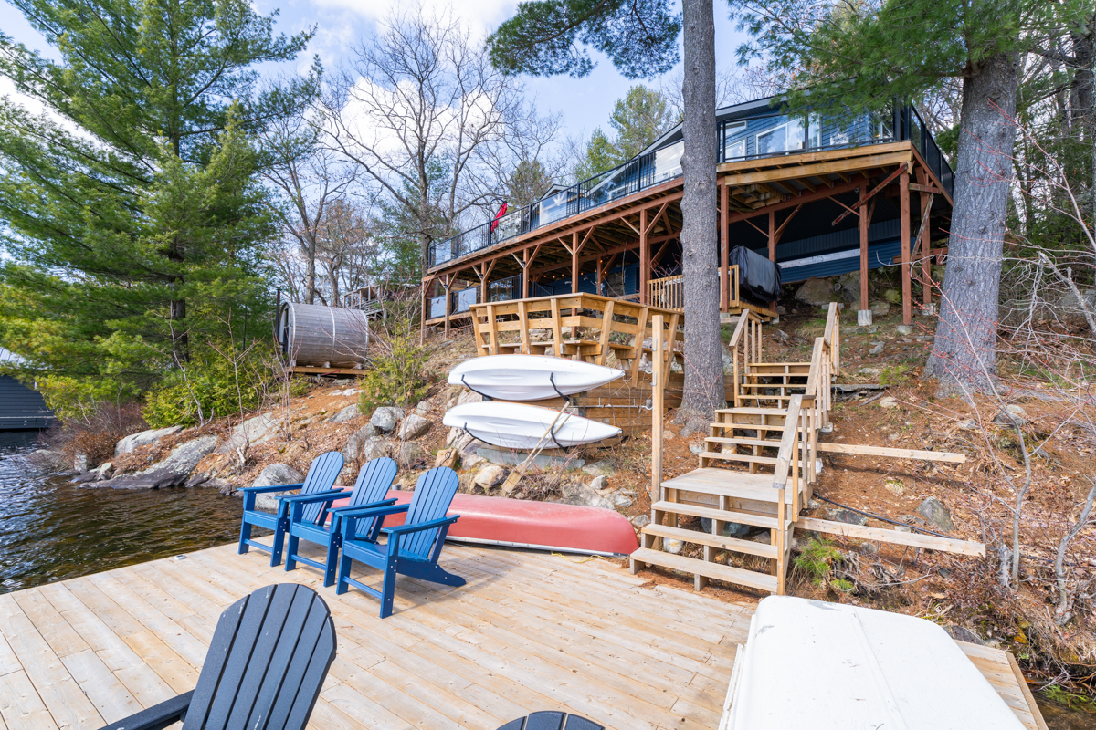 View from the dock. Blue Muskoka chairs and a red canoe sit on the dock