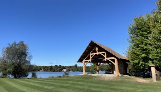 A gazebo by a wide grassy space and a lake