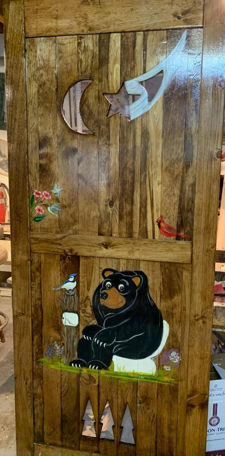 A brown outhouse door with black bear sitting on the toilet