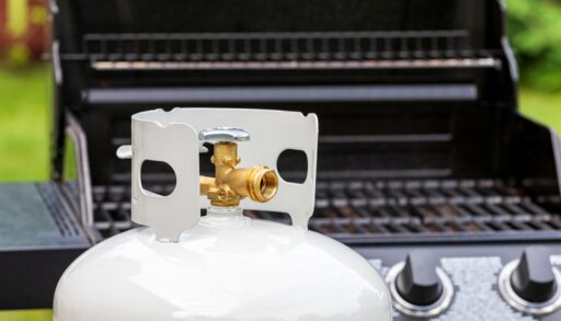 A propane tank with a barbecue in the background