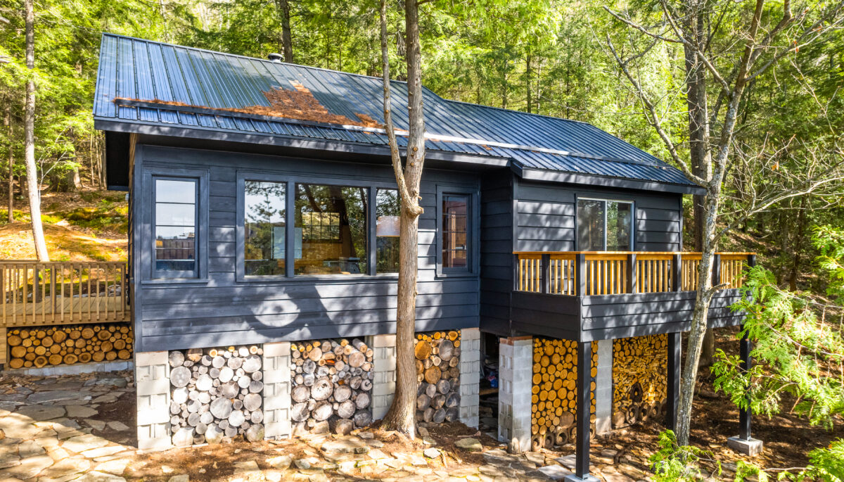 A dark grey panelled cottage with a base made of cut logs