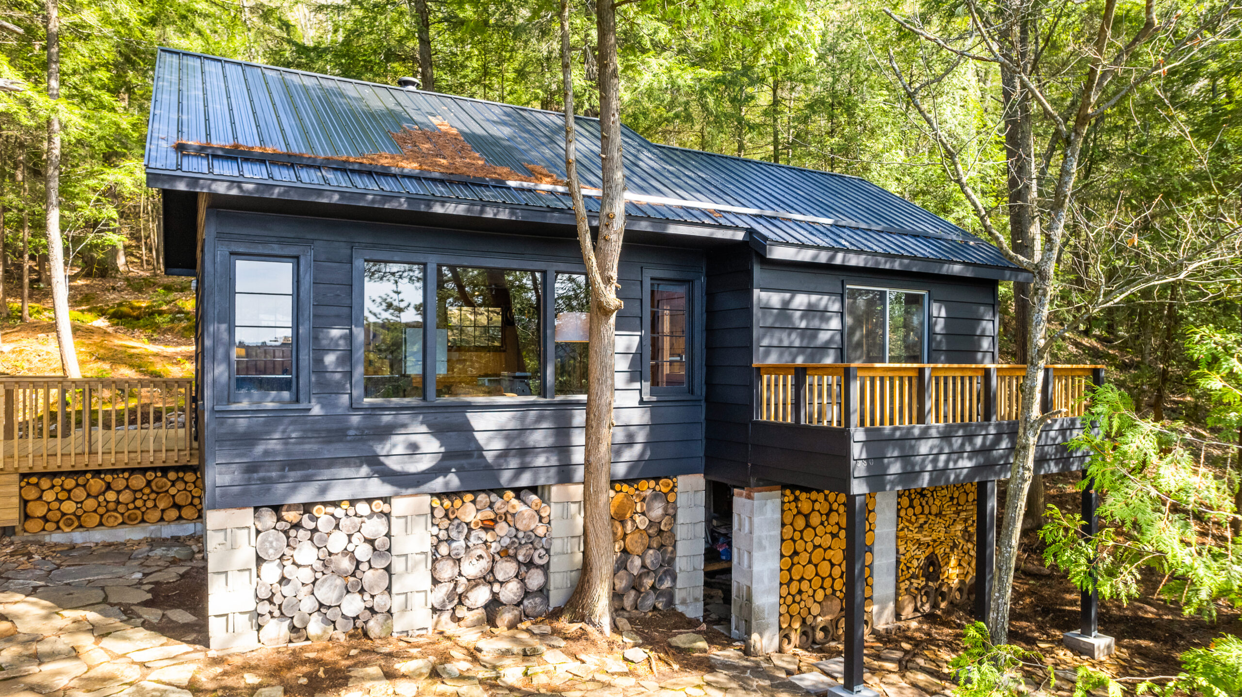 A dark grey panelled cottage with a base made of cut logs