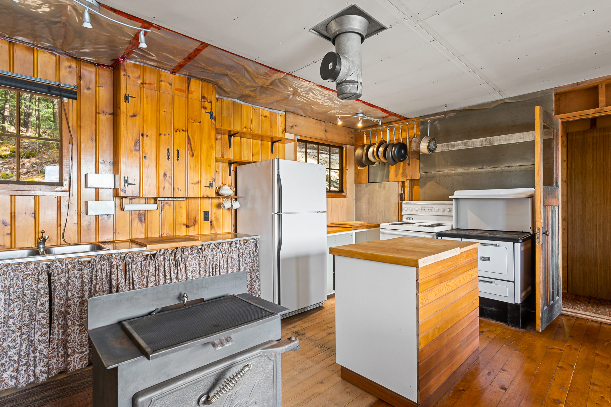 Wood panelled walls in the kitchen. A small white ktichen island and white appliance line the walls