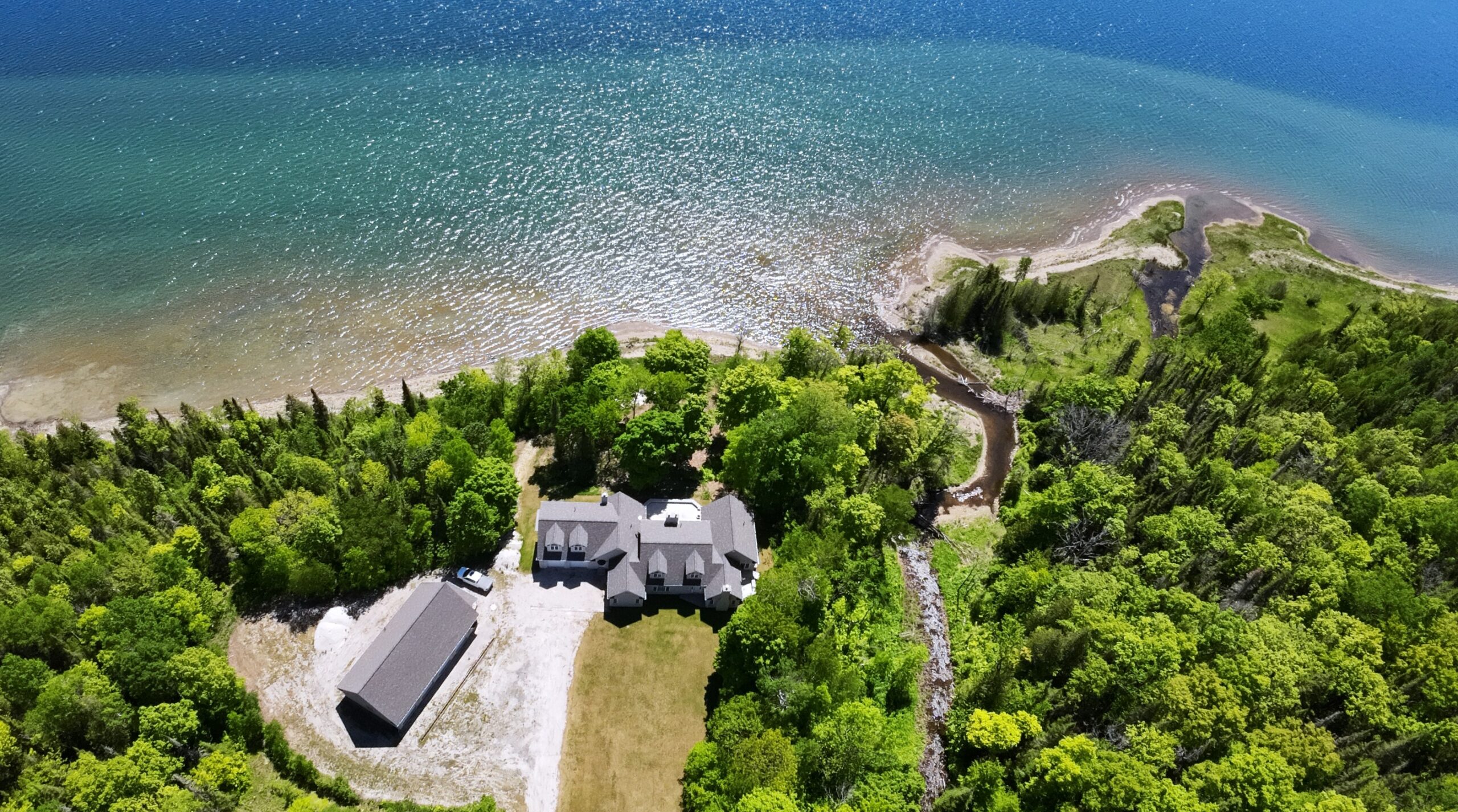A large house on a huge property surrounded by green trees. A blue lake behind