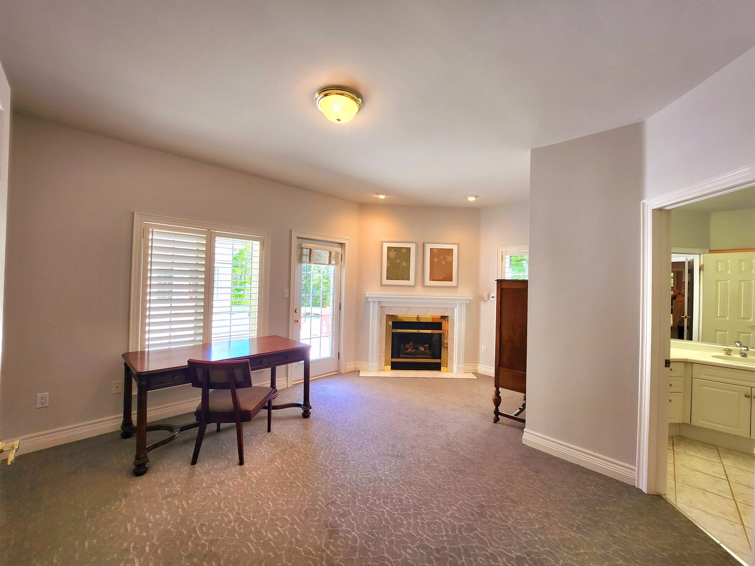 An empty room with a small desk facing a window. To the right, a fireplace