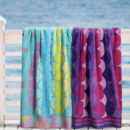 Two towels hanging on a fence at the beach, one blue/green and one purple/pink