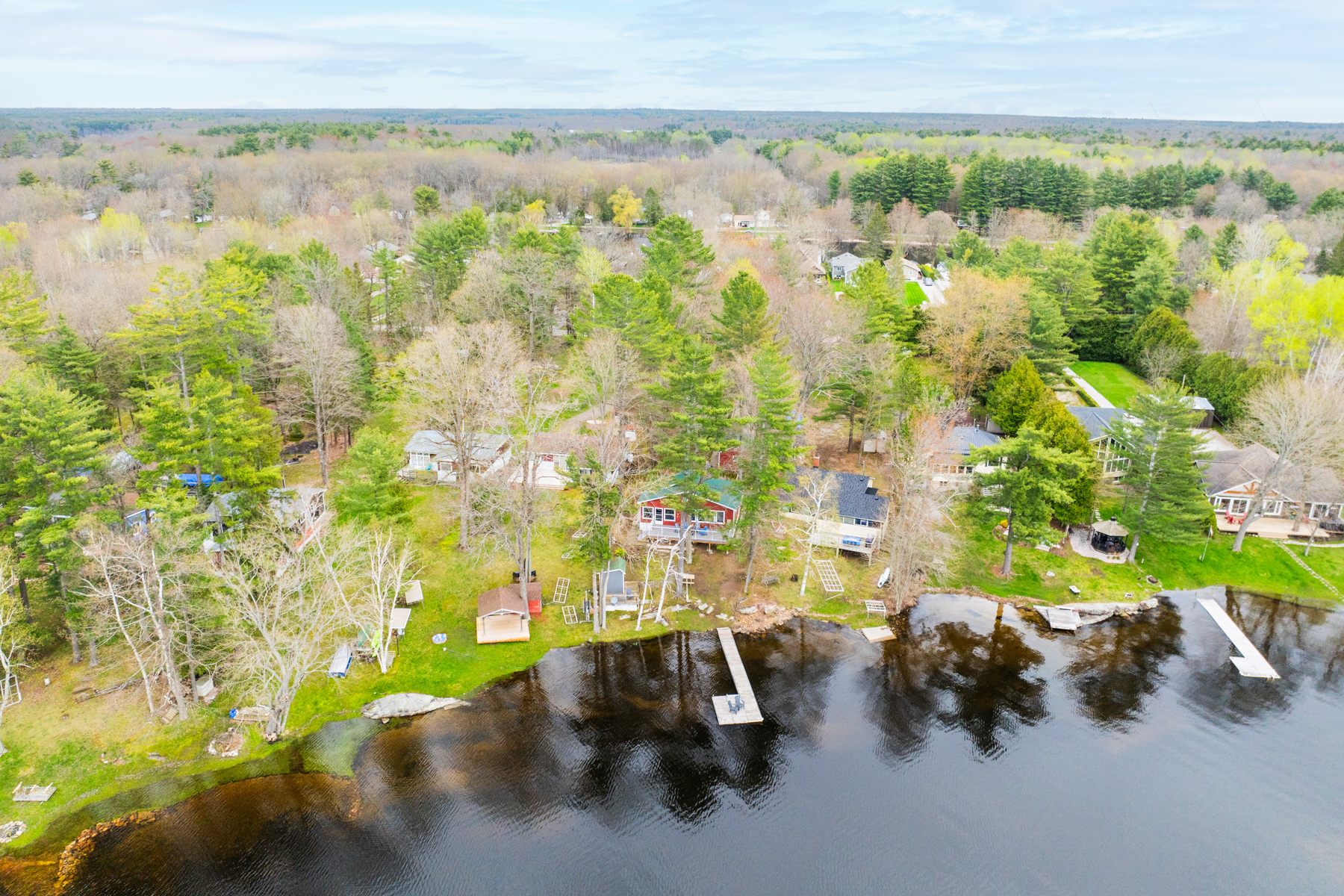 Cottages line the shore of a still lake. A couple of long docks extend into the water.
