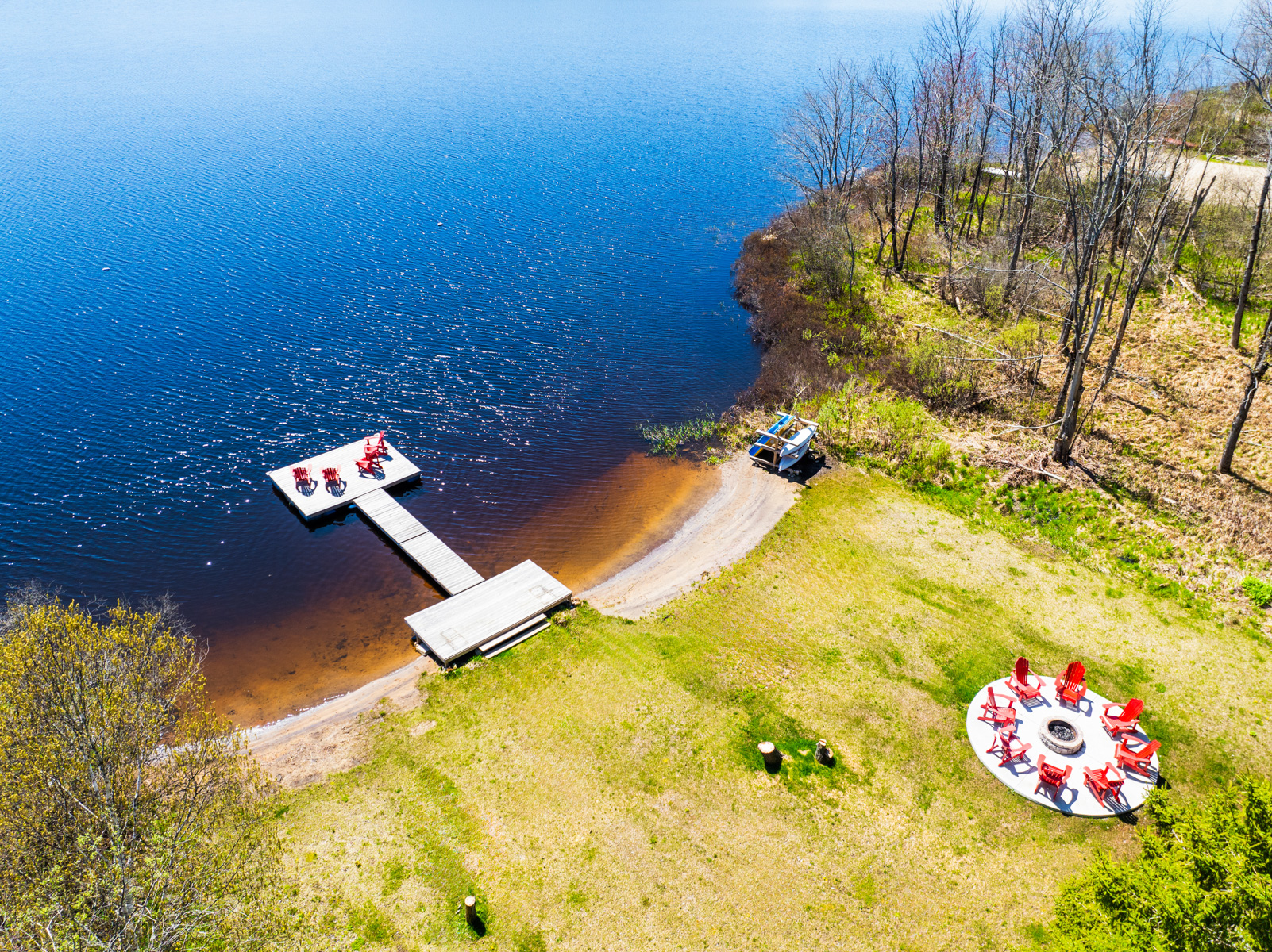 Aerial view of property shows a large section of yellow-green grass with a fire pit that lines up with the blue lake