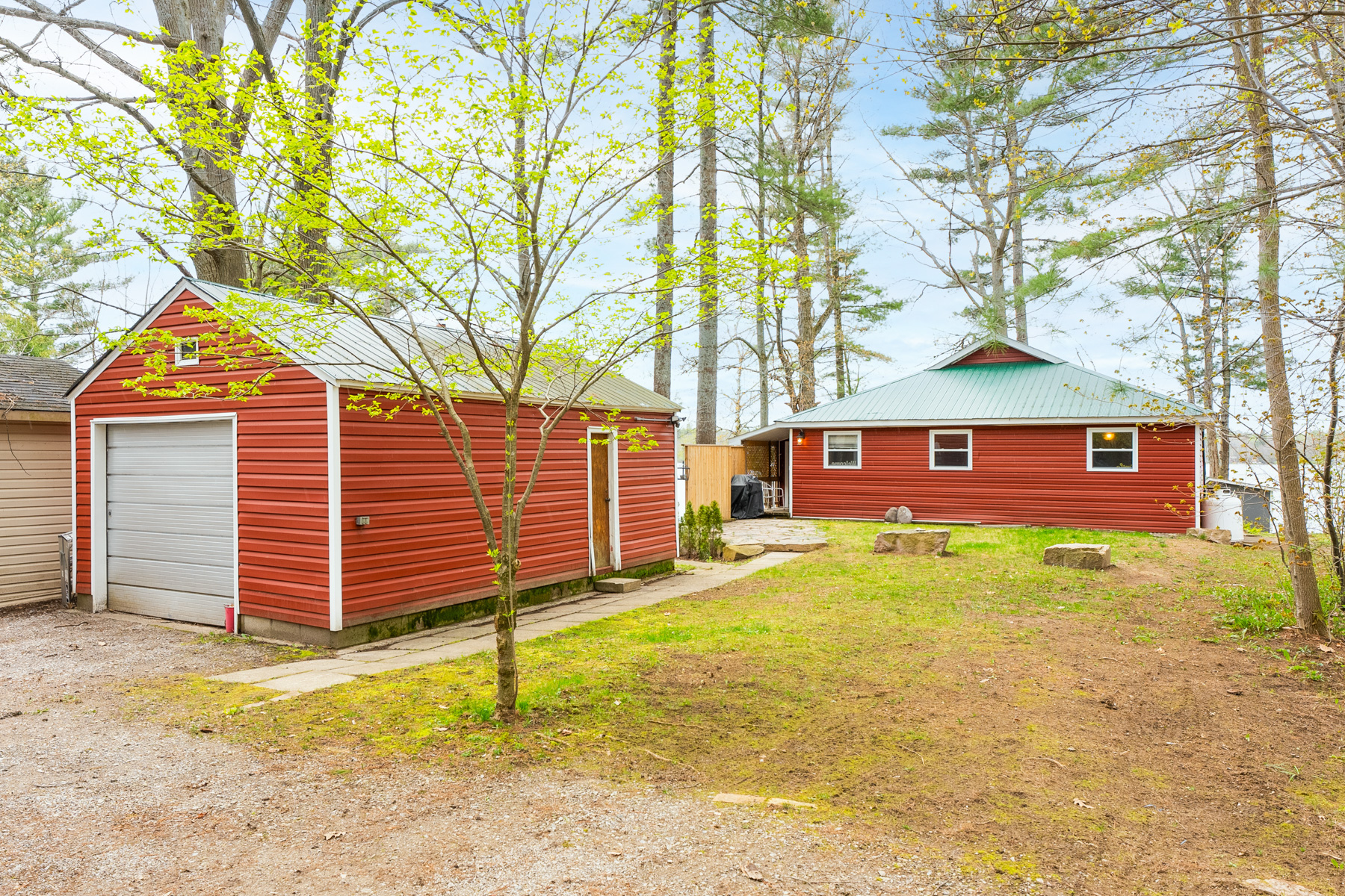 A grassy lot with a red detached single garage in front of a red cottage bungalow.