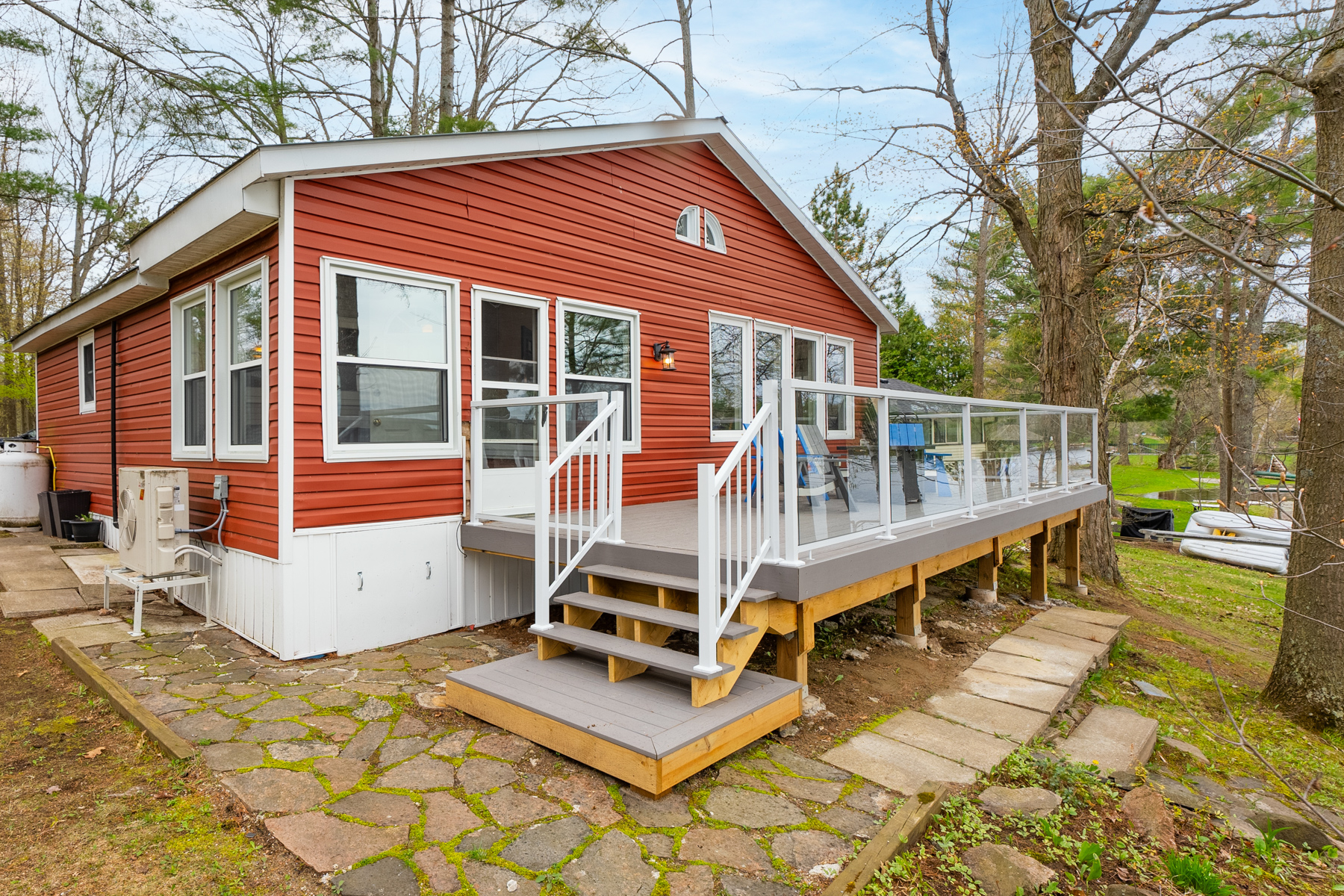 A cottage bungalow with red siding and lots of windows. A new deck with a glass railing spans the back of the cottage.