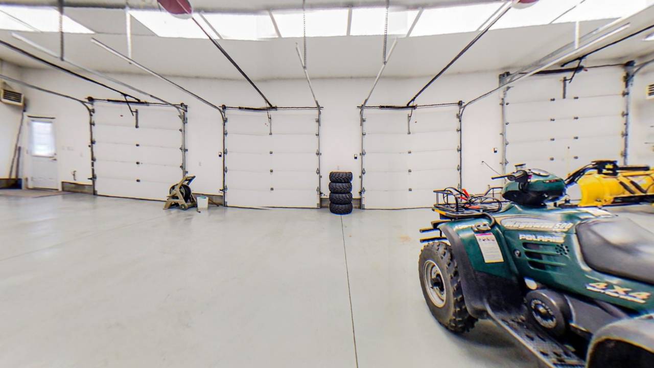 Inside a large white garage, the front of a car faces the garage doors