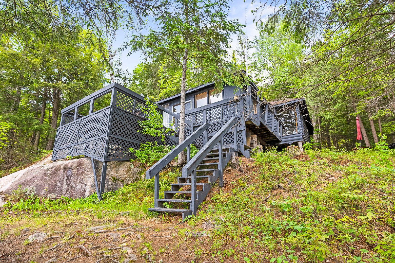 Steps lead up to a dark grey cottage surrounded by trees