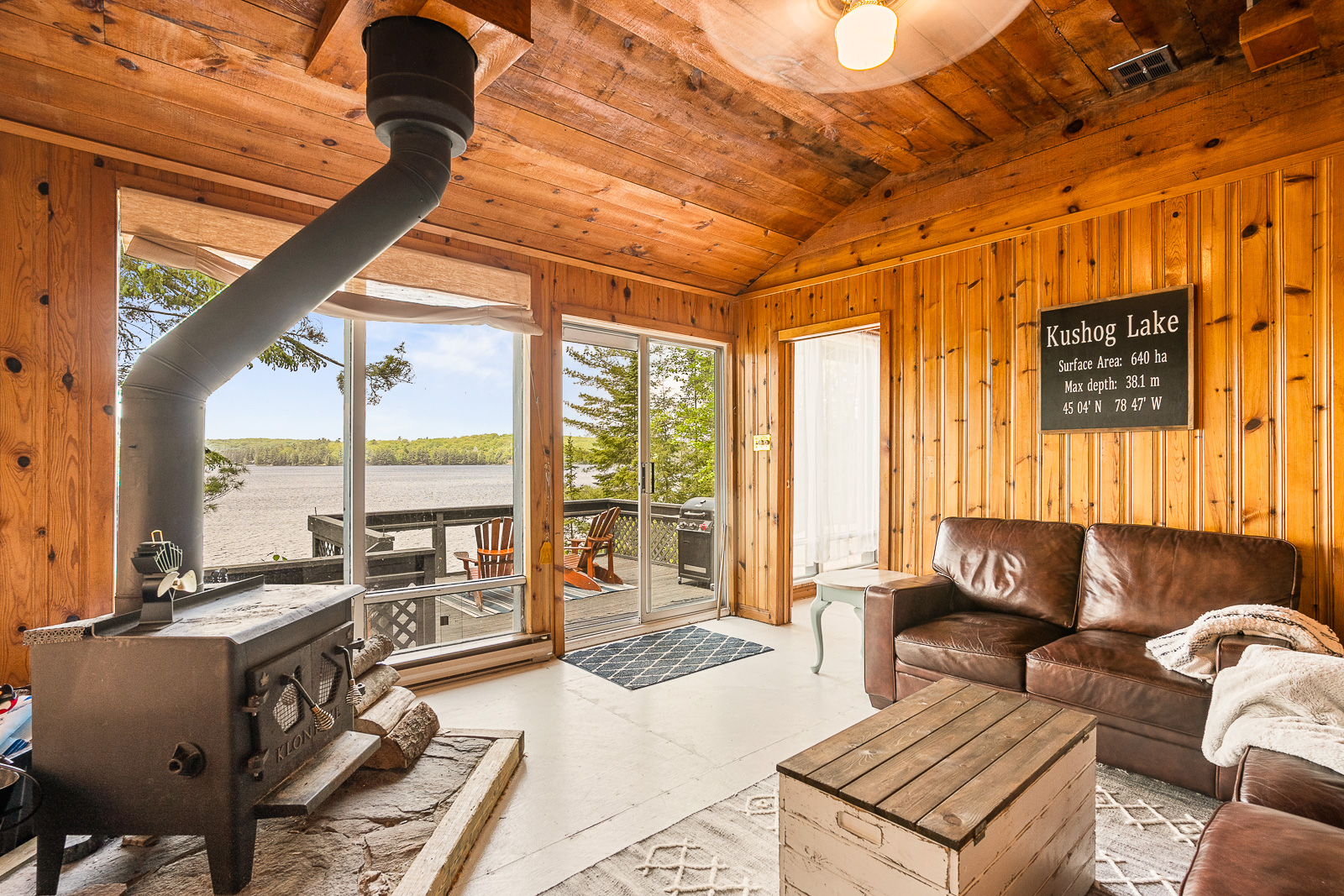 A woodstove on the left faces a brown leather couch and table. They all face bright sliding doors that lead out to the deck