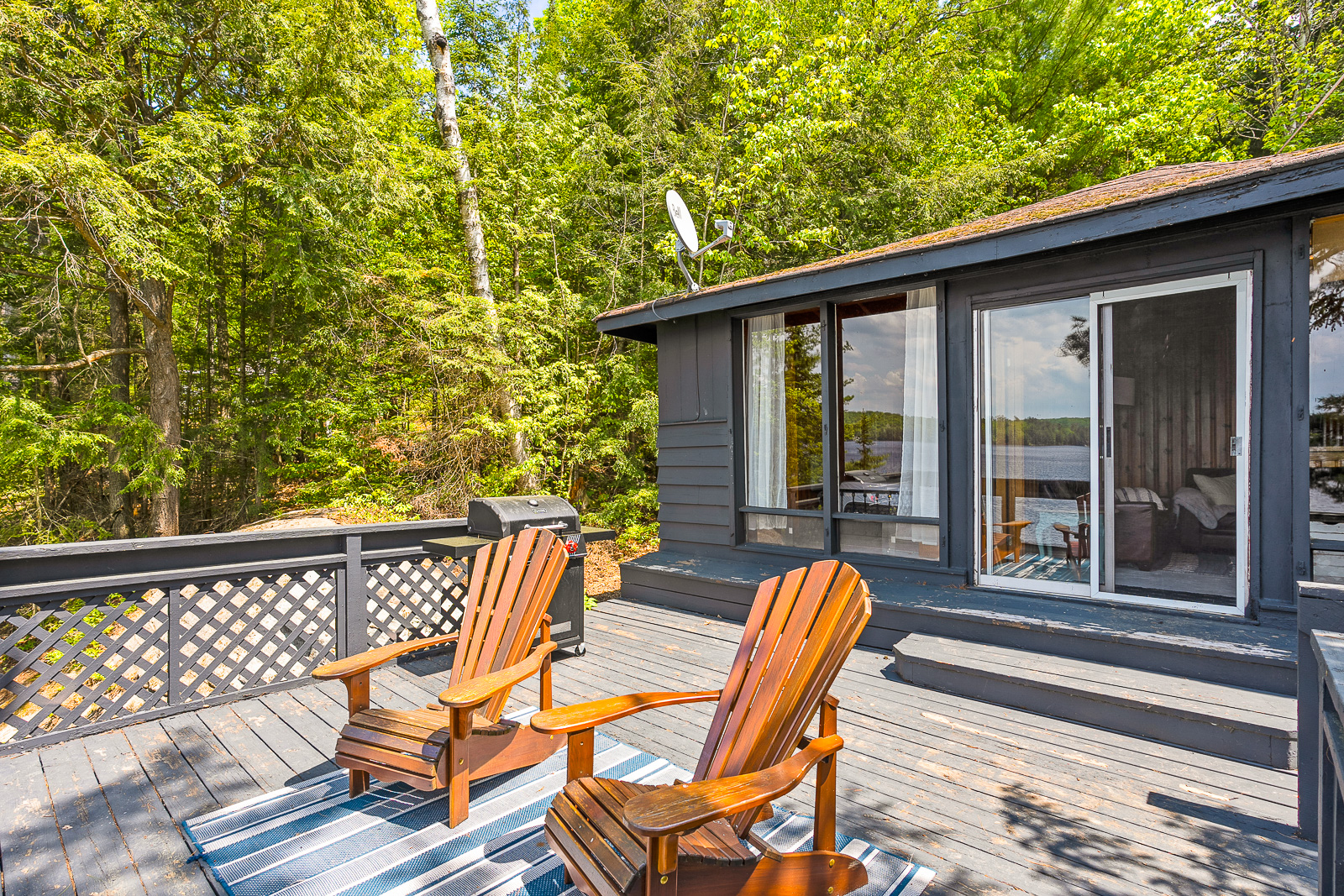 In front of the dark grey cottage, two brown Muskoka chairs on the deck