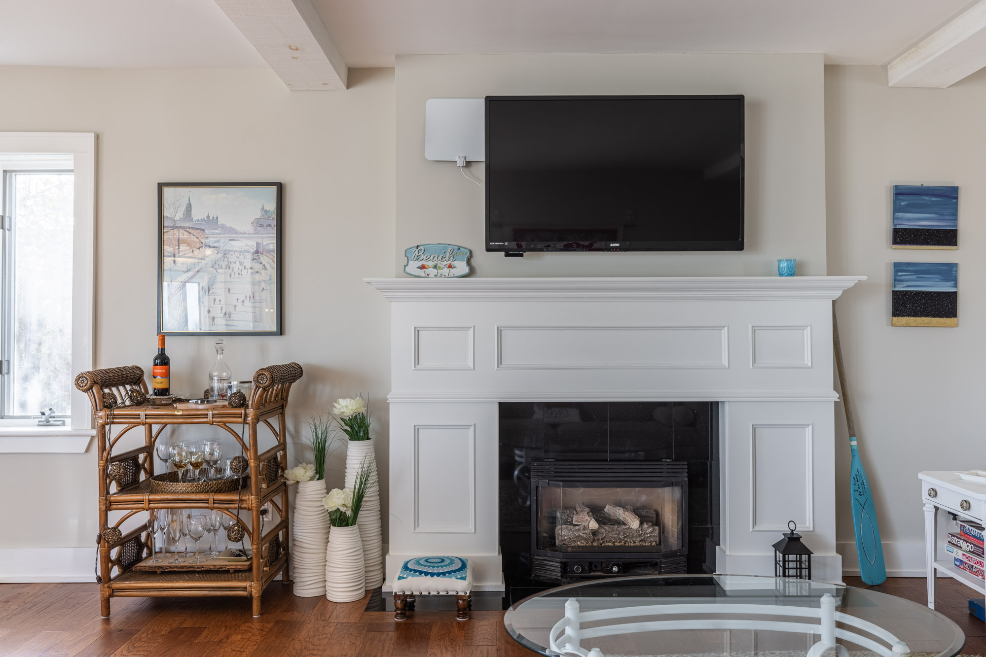 A white trimmed fireplace with a TV hanging above, next to a small bar cart