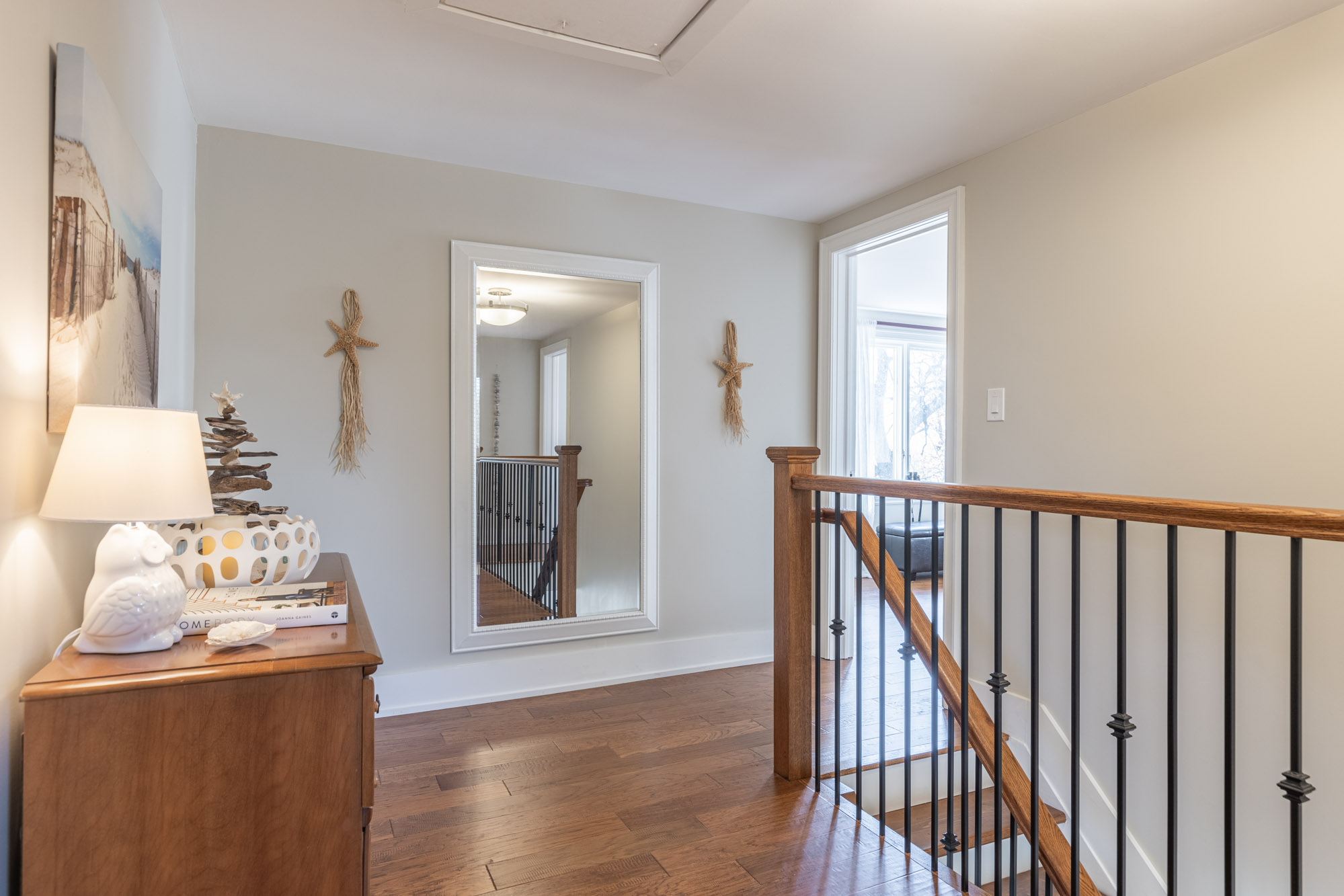 Second floor landing with brown hardwood floors and a large mirror facing the stairs