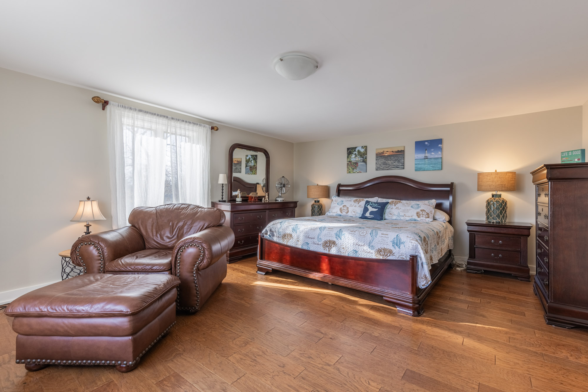 A large white bed next to a brown leather chaise lounge