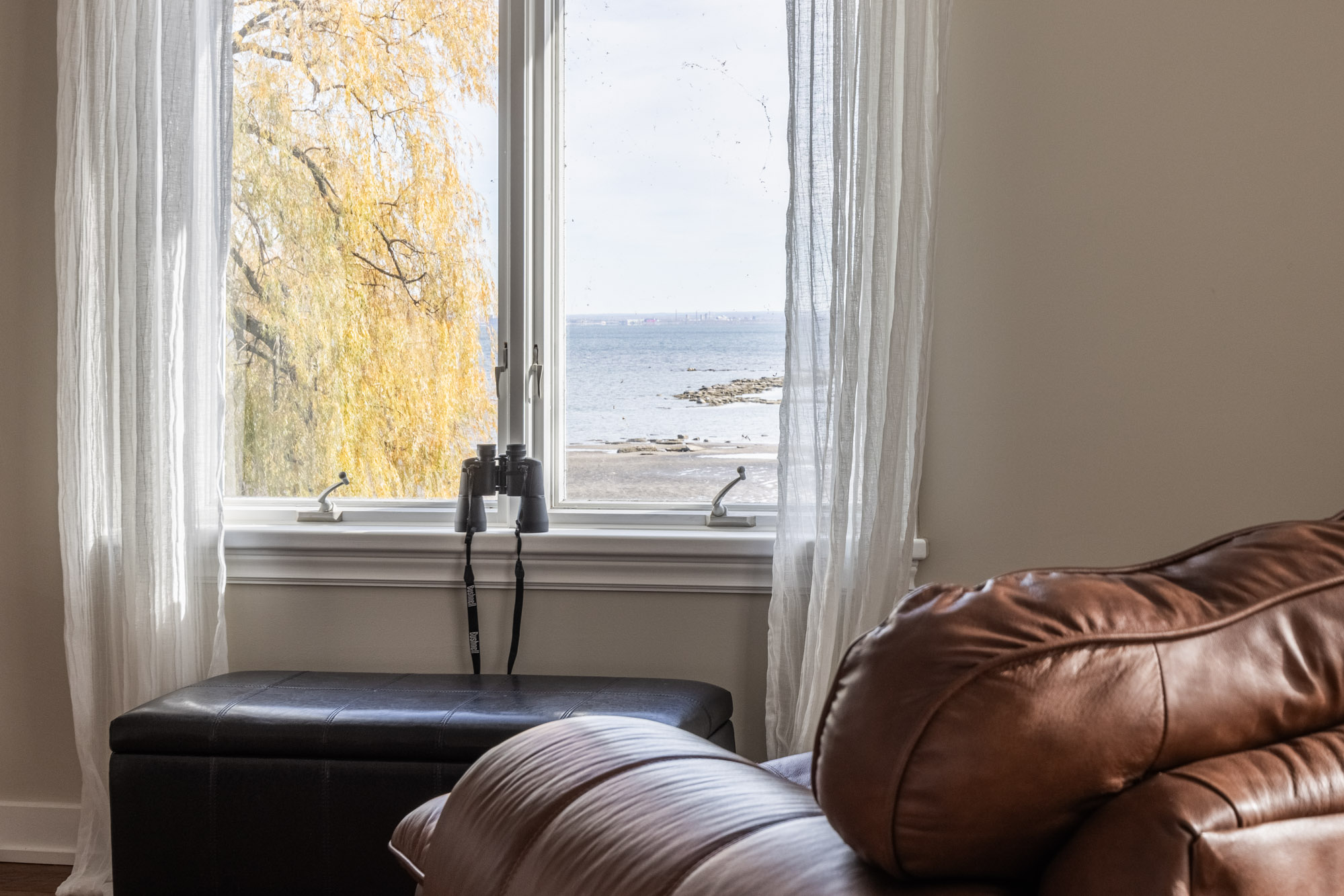 A bright window, with binoculors sitting on the window sill, looks out onto the lake