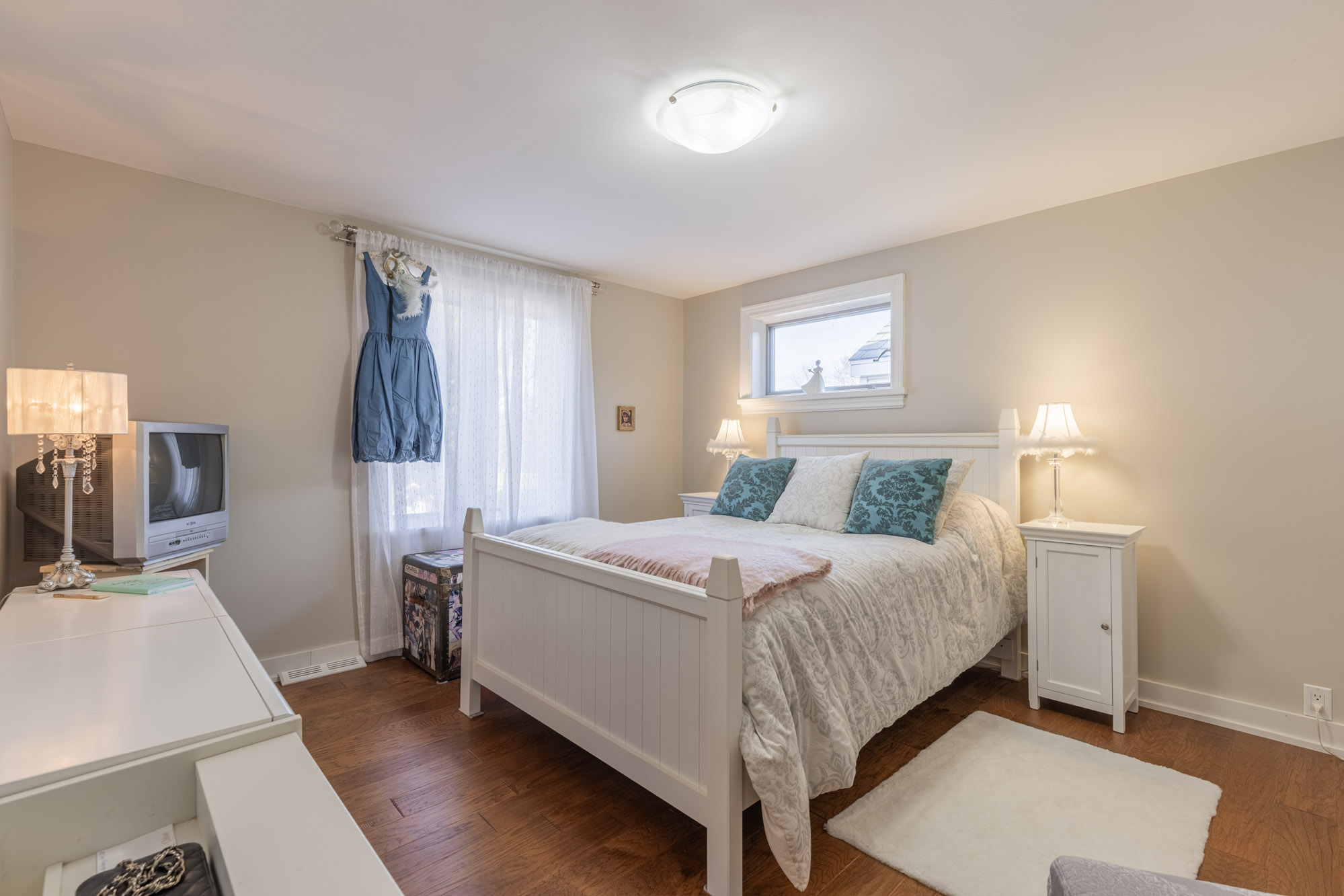 A white bedroom with a white bed faces a white dresser
