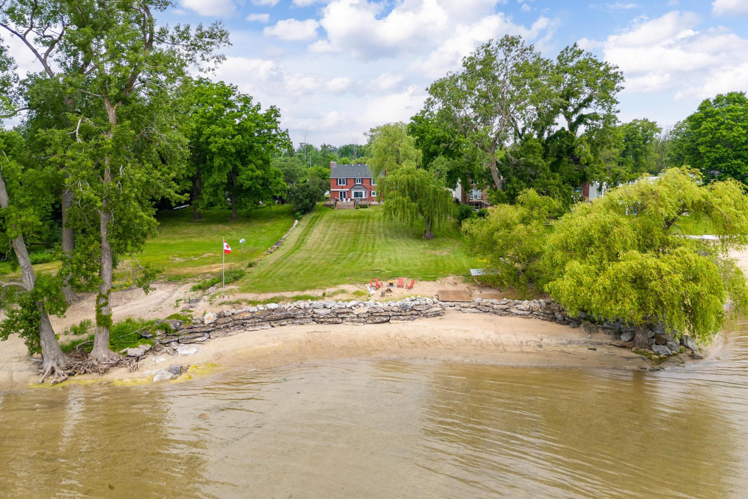 Brown water on a beachfront that leads to a grassy backyard with the red brick house in the distance