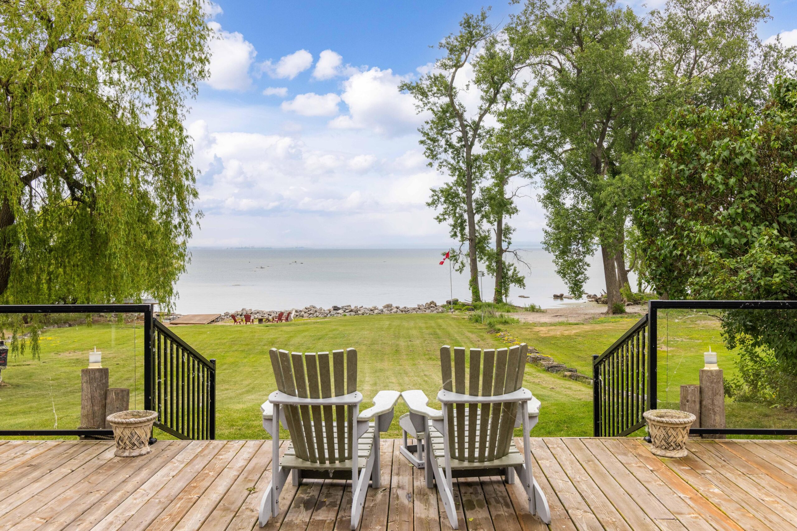 Two Muskoka chairs on the deck face the grassy backyard and lake