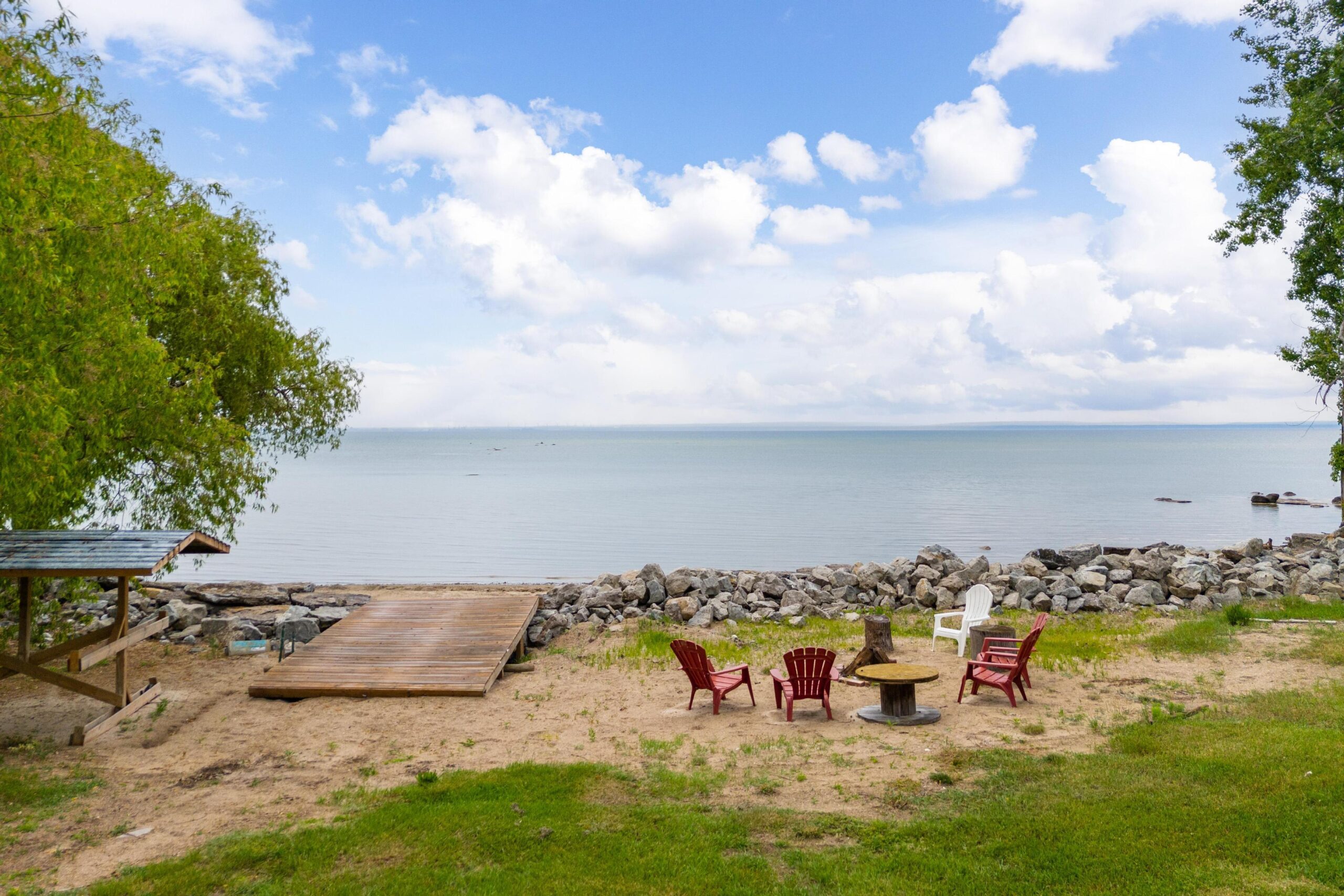 A dock and red Muskoka chairs on the beach face the lake