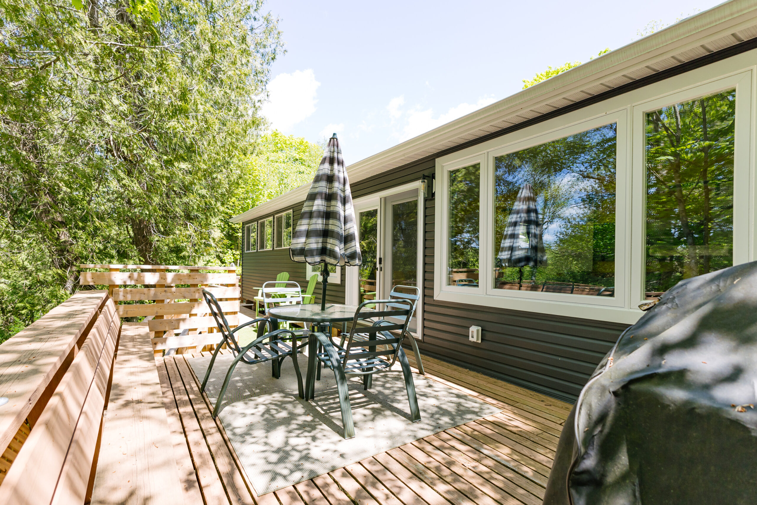 A white glass table and chairs with a closed striped umbrella on the back deck.