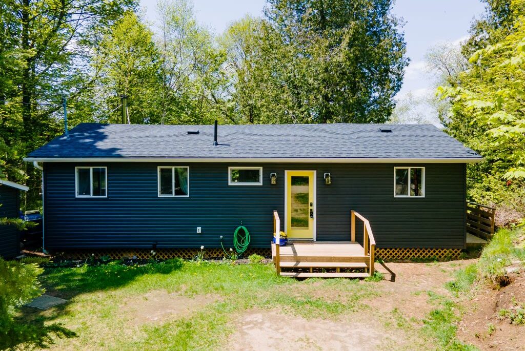 A blue-grey panelled bungalow with wood streps that lead to a bright yellow door