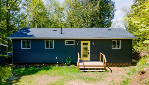 A blue-grey panelled bungalow with wood streps that lead to a bright yellow door